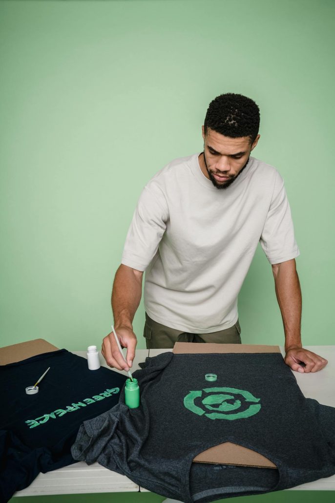 Man with beard painting custom designs on t-shirts in a studio setting.